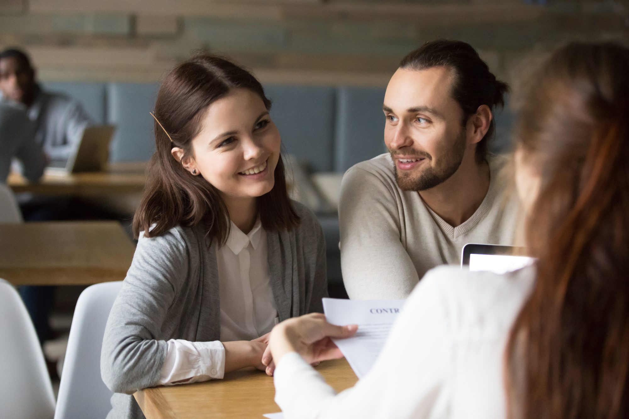 Happy millennial couple planning to sign mortgage contract meeting realtor, smiling clients considering real estate deal, buying insurance, investing money being consulted by financial advisor broker