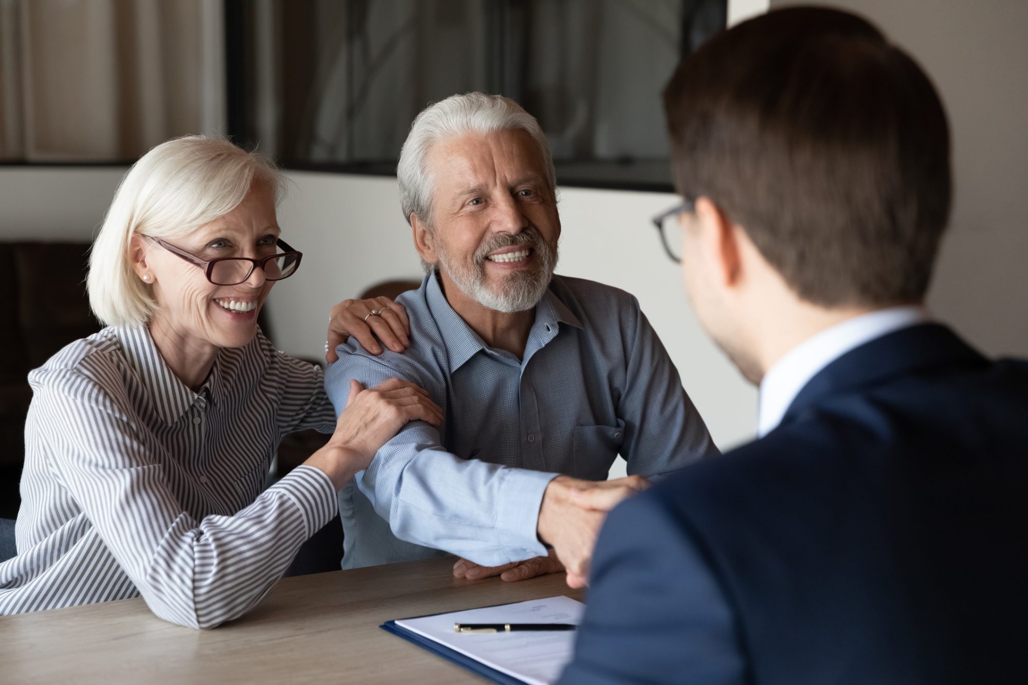 Smiling older Caucasian man and woman clients shake hand greeting get acquainted at meeting with specialist. Happy mature couple customers handshake close deal with real estate agent or broker.